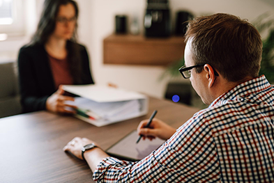 Ein Steuerberater im Gespräch mit einer Mandantin, konzentriert auf die Durchsicht von Finanzdokumenten und Steuerunterlagen – Professionelle und persönliche Steuerberatung in Aktion.